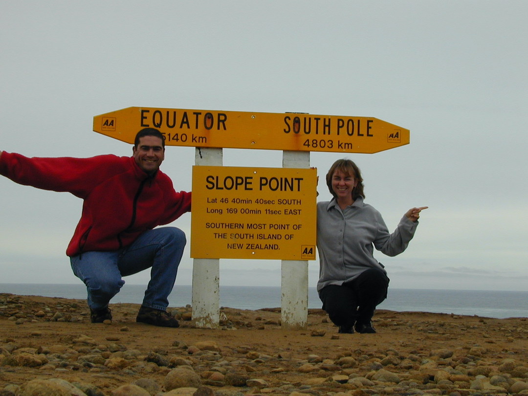 Schindlers on Tour at Slope Point New Zealand David and Sharon Schindler sitting at Slope Point sign in New Zealand